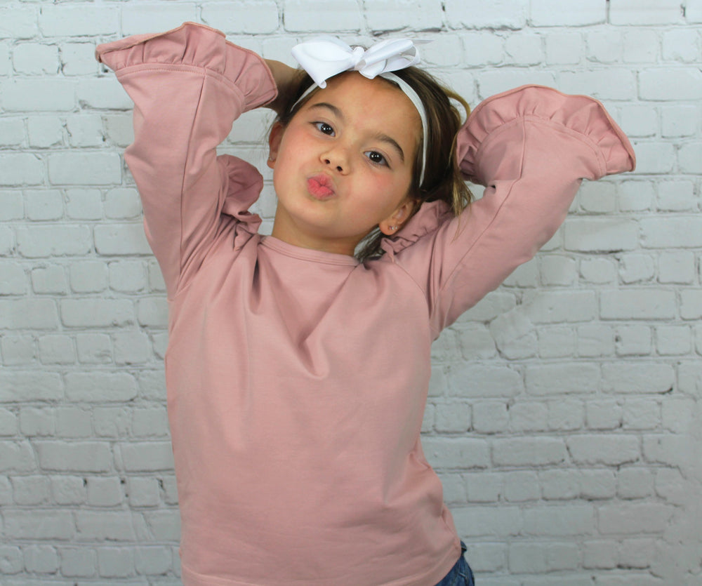 The Ruffled Sleeve Top is such a beautiful blouse that can be worn by our baby diva's all the way up to our tween girls! The ruffle design lines the outer and inner part of the sleeves making it super fashionable. The color of the blouse is a blush pink which pairs nicely with jeans or black pants.